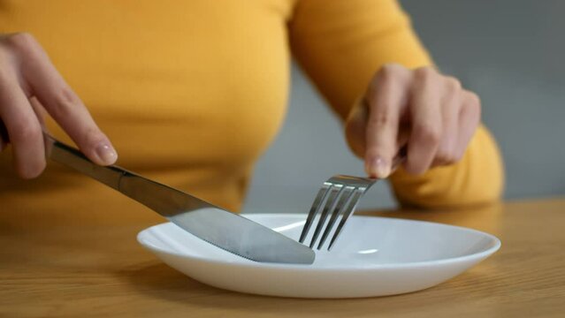 Poverty concept. Hungry unrecognizable lady cutting imaginable food with knife and fork in empty plate, slow motion