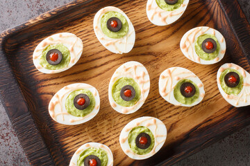 Funny Halloween food eyeballs deviled eggs stuffed with avocado cream on a wooden tray on the...