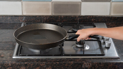 A woman's hand holds a frying pan with oil on a gas stove