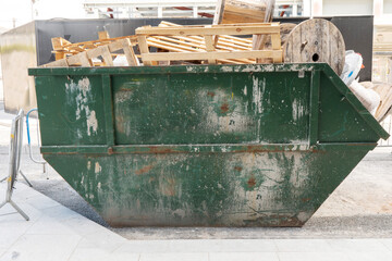 Green metal skip full of construction site rubbish and electric cable reels ready for collection in...