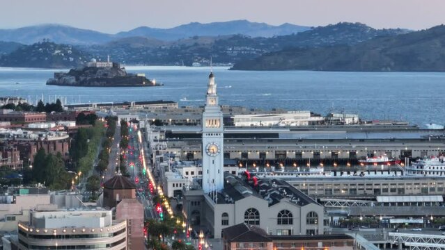 Cinematic aerial shot of historic landmark Ferry building tower, Embarcadero in San Francisco with Alcatraz island on motion parallax background. Bay bridge appear on foreground in dawn sunrise light