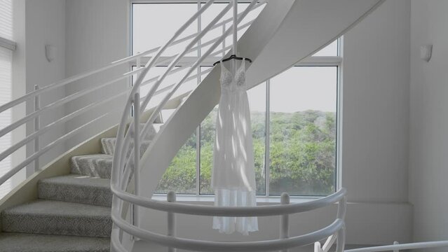 Sunlight shines on bride's wedding dress hanging. Dolly Out Shot