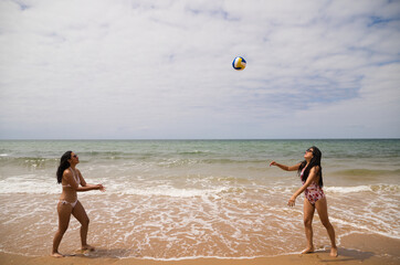 Two young and beautiful women playing boley on the shore of the beach. The women are enjoying the game and their day at the beach in paradise. Holidays and travels.