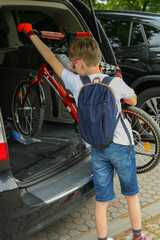 Fototapeta na wymiar A boy pulling a bicycle out of a car trunk