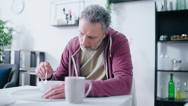 Unhappy mature man having breakfast, midlife crisis, hangover morning, miserable