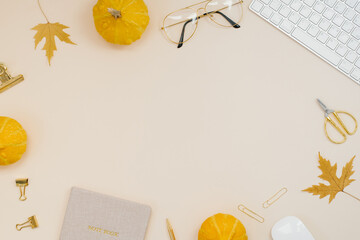 Workplace computer with yellow maple leaves and pumpkins, glasses, scissors, notepad, pen, clips, paper clips on a light beige background. Flat lay, top view. Work office desk with autumn blogger 