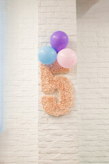Pink number 5 and balloons are hanging on a white brick wall. The decor of the children's room for the child's birthday