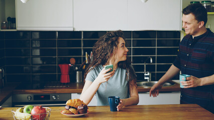 young happy positive caucasian couple in love meeting in the morning in modern kitchen at table to...