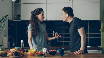 Pretty woman standing at table cutting salad while her boyfriend comes and they argueing speaking loud and nervous. Relations , difficulties concept