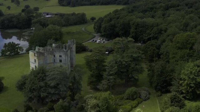 Moody, dark, evening drone flight over Old Wardour Castle ruins near a lake.