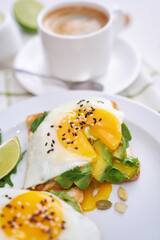 healthy breakfast or snack - sliced avocado and fried egg on toasted bread and cup of coffee