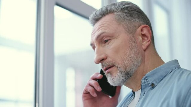 Middle-aged man talking on the phone with his ex, arguing over divorce, anger