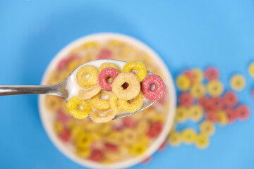 Cereal rings with milk, close-up in spoon, top view, blue background.