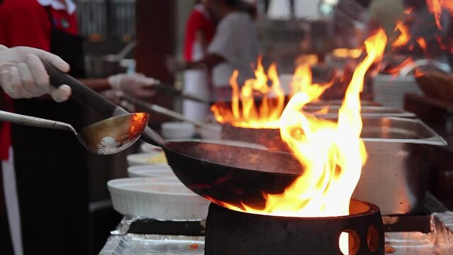 Team Of Chefs Cooking In Front Of Hotel Guests In Outdoor Kitchen. Chef Flambe Cooking - Stir Fry Cooking In Flaming Pan.
