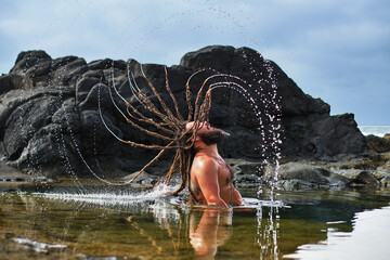 rasta boy shaking his wet hair in the sea at sunset