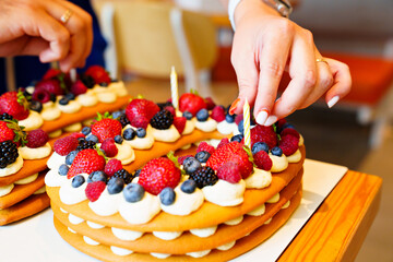 candles put on the cake with berries in the form of the number ten.