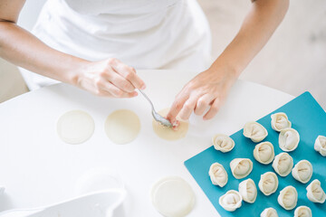 Obraz na płótnie Canvas Woman making dumplings. Front view of woman's hands making meat dumpling. Cook hands lay out minced meat on dumplings