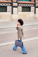 smiling latin business woman walking across the street talking by phone with a briefcase in her hand, concept of urban lifestyle and success, copy space for text