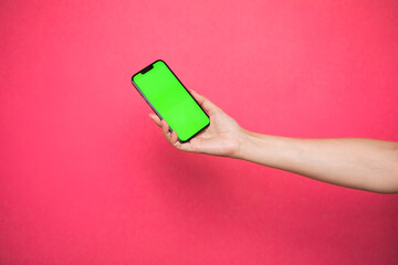 Woman hand Holding a Green Screen Smartphone on pink background.