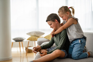 Little girl and boy watching video or playing games on their digital device tablet, smartphone.