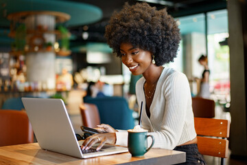 Smiling young african woman sitting with laptop in cafe