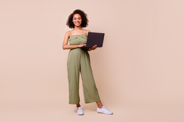 Full length photo of funny brunette woman work laptop wear khaki overall isolated on beige color background