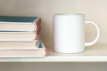 Fototapeta na wymiar A white mug on a bookshelf near a stack of books