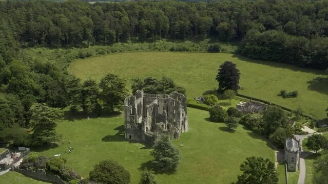 Old Wardour Castle ruins surrounded by bright green fields and forest. High angle.