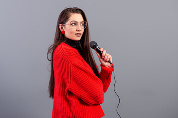 young, emotional brunette with a microphone dressed in a red sweater sings karaoke or says a speech