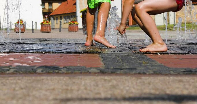 Children playing in water fontain on a hot sunny day in a heat wave at a city park.