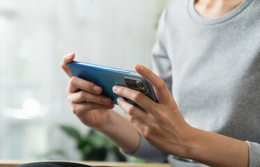 Woman hands playing video game on smartphone and sitting on sofa in living room.