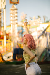 Young cute girl with pink hair posing on the background of the rides. Charming hipster girl