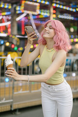 Cute girl eating ice cream. A girl with pink hair poses with ice cream. Stylish girl in a yellow top. Attractions on the background