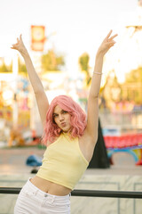 Young cute girl with pink hair posing on the background of the rides. Close portrait Charming hipster girl at sunset smiling