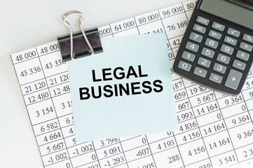 LEGAL BUSINESS text on a blue card that lies on a sheet with reports next to the calculator on the table, business concept