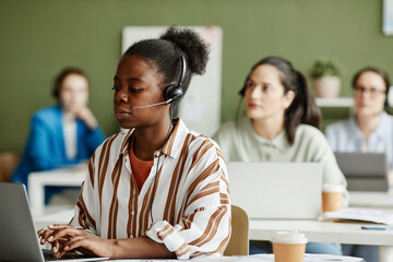 African young female operator in headphones working at her workplace with laptop at call center