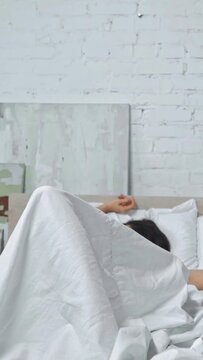 vertical video of happy woman waking up and adjusting hair while smiling in bedroom