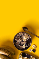 Top view of homemade granola bowl with unprocessed whole grains, chia, quinoa, nuts, seeds with chocolate slices on yellow background.