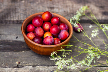 Ripe cherry plum in a round brown ceramic plate on a wooden background. Summer composition in the village, harvesting