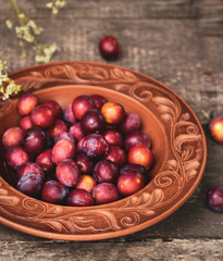 Ripe cherry plum in a round brown ceramic plate on a wooden background. Summer composition in the village, harvesting