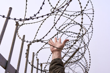 A man's hand against a background of barbed wire. The concept is repression, migration.