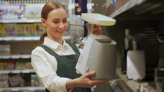 Young woman buyer discovers quality of white food processor. Satisfied lady examines modern device and wants to make purchase for kitchen in supermarket closeup