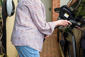 Mature woman using electric charging point at home to fuel electric car