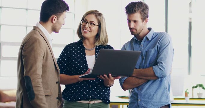 A group of formal businesspeople talking together about ideas over a laptop in a modern office. Female manager using interactive screen to show coworkers their project and discussing it for deadline
