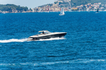 Fototapeta premium Blue and white luxury speedboat or yacht in motion on Mediterranean sea in front of the Porto Venere or Portovenere, Gulf of La Spezia, UNESCO world heritage site, La Spezia, Liguria, Italy, Europe.