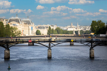 Photograph of the Pont des Arts over the Seine river in Paris, dividing the Parisian city in two parts. Creating a beautiful scenery with the bridge and the Parisian city in the background.