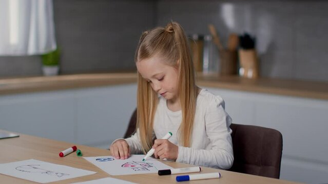 Kids and creativity. Adorable little girl drawing picture with colorful markers, sitting at kitchen, empty space