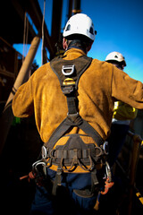 Back side of international rope access male welder wearing a safety helmet and harness over welding leather fire clothing protection jacket uniform on construction building site Perth city, Australia