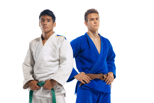 Portrait of two young men in white and blue kimono, martial arts athletes posing isolated over white studio background