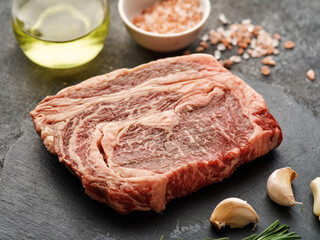 Raw ribeye steak on a black board with garlic and rosemary. Fresh marbled beef
